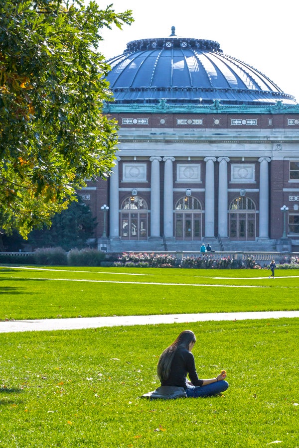 Female student sitting on the Main Quad in front of Foellinger Auditorium in early fall. 