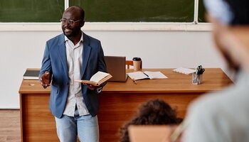 Teacher standing with book and reading lecture for students at university